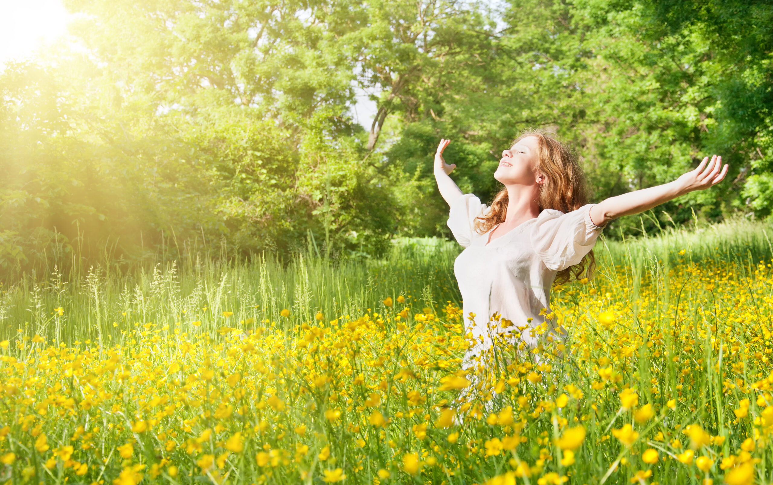 Eine Frau genießt die Sonne mit offenen Armen in einer Blumenwiese